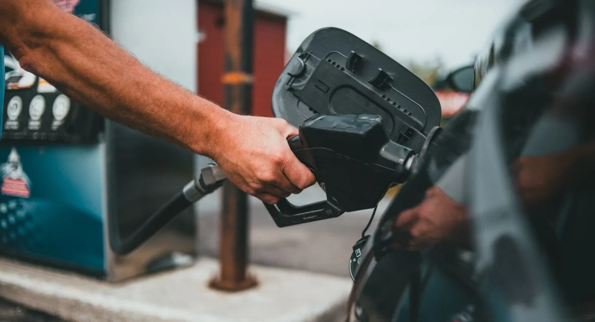 Close-up of a hand holding a nozzle while refueling a car at a gas station.