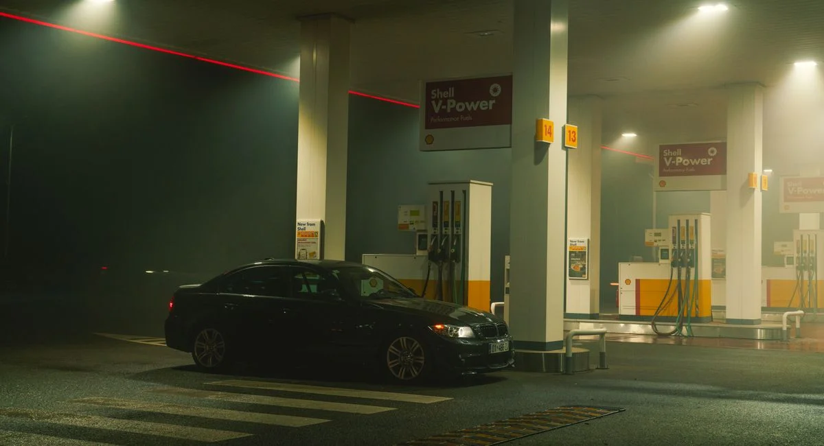 A BMW sports car parked at a Shell gas station at night, featuring bright lights and an urban setting.