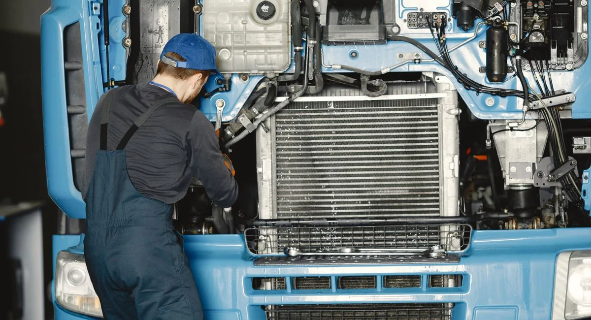 Mechanic in uniform working on a truck engine in an industrial workshop. Perfect for automotive maintenance themes.