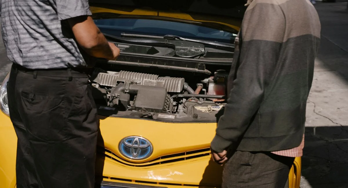 Back view of crop anonymous males checking details of engine under hood of cab in New York