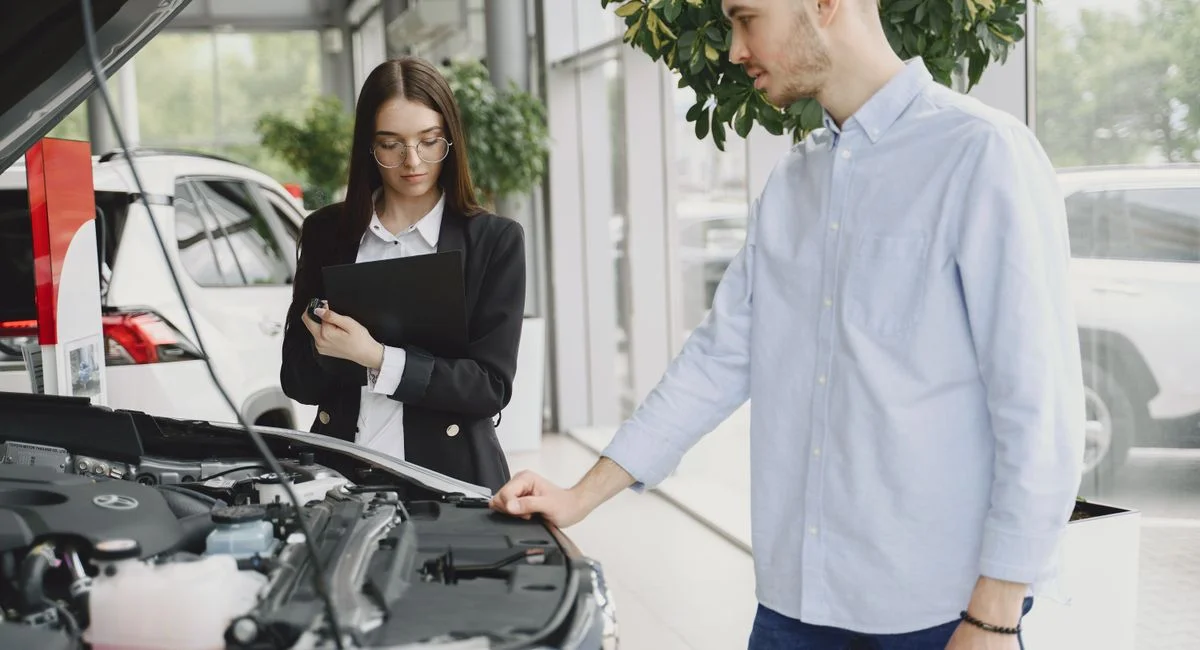 Man and woman examining car engine in dealership service area, focused on vehicle maintenance and functionality.