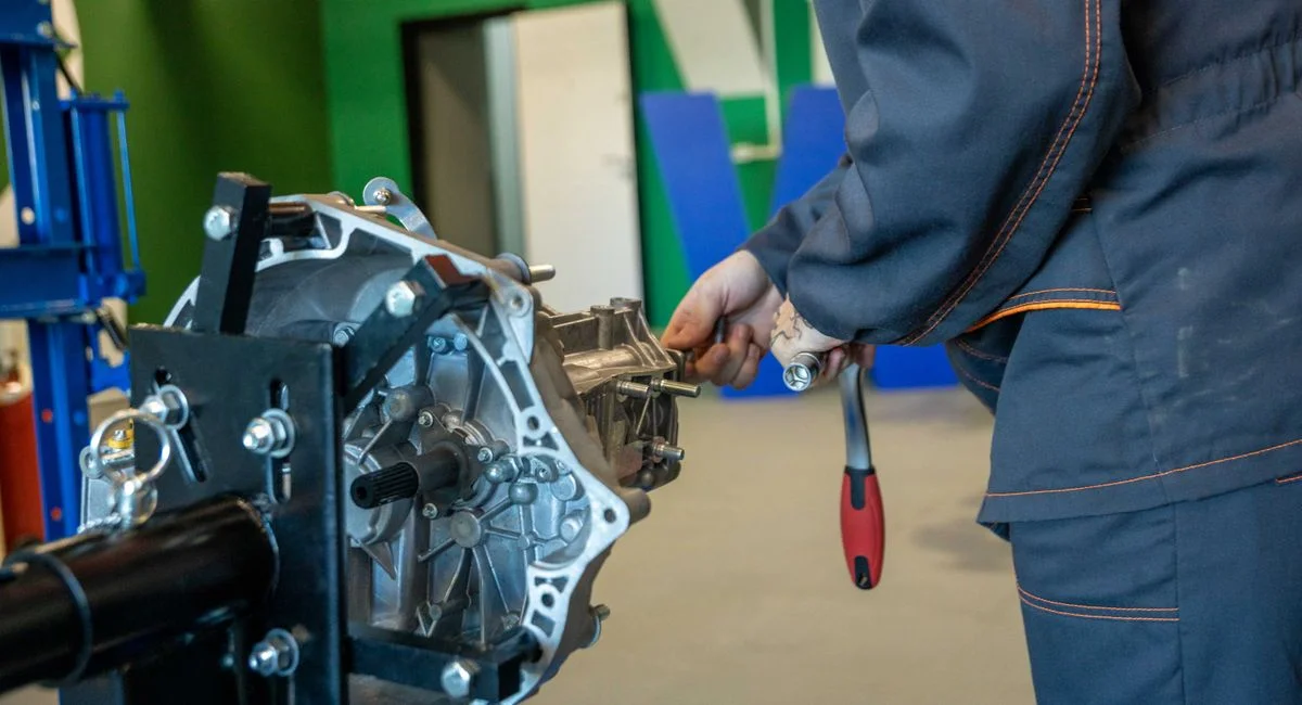 Mechanic uses tools to repair car transmission in an indoor workshop setting.