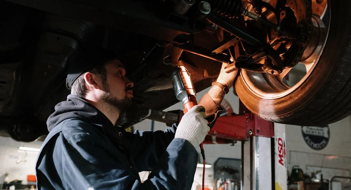 Mechanic examining car's undercarriage at a garage, focusing on vehicle maintenance.