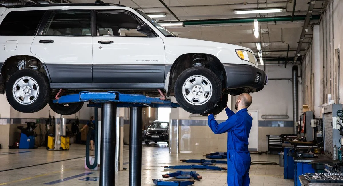 A mechanic inspecting a white SUV lifted in a well-lit auto repair shop.