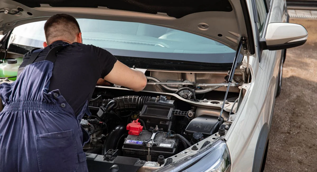 A mechanic fixes a car engine outdoors, focusing on vehicle maintenance.