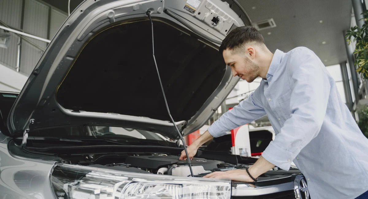 A man in a blue shirt examines a car's engine in a modern vehicle showroom.