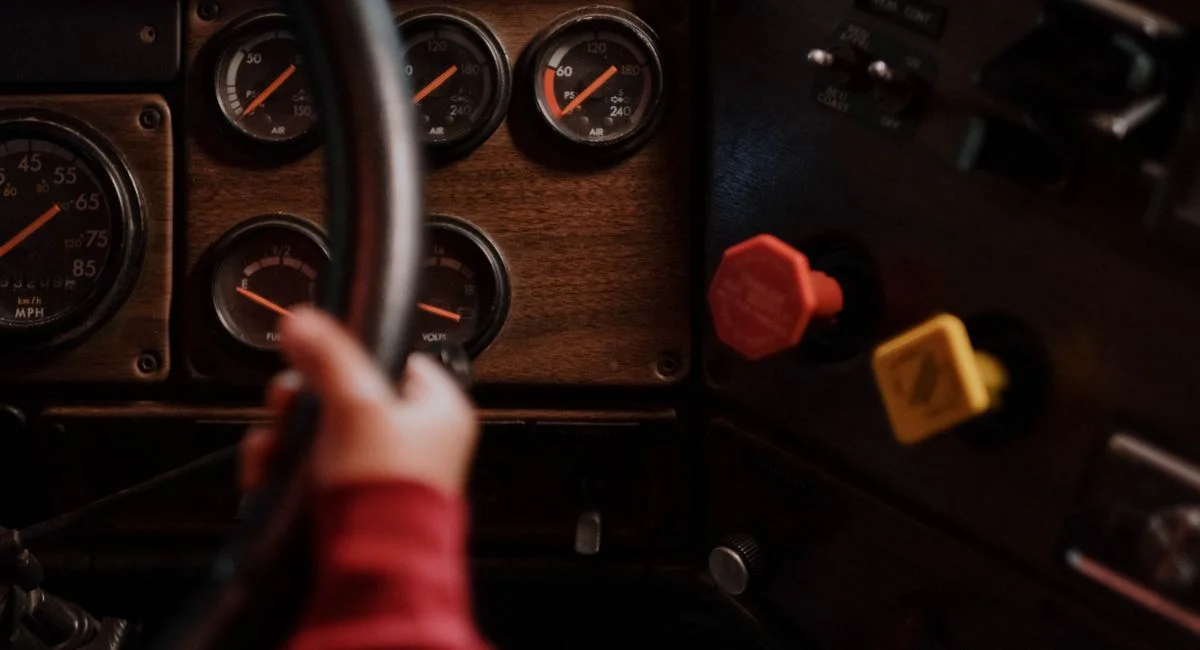 A child’s hand gripping a steering wheel in a vintage vehicle interior with dials.