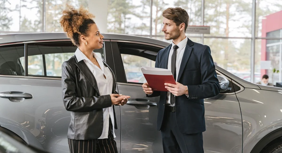 A woman discussing car purchase with a dealer inside a car dealership showroom.