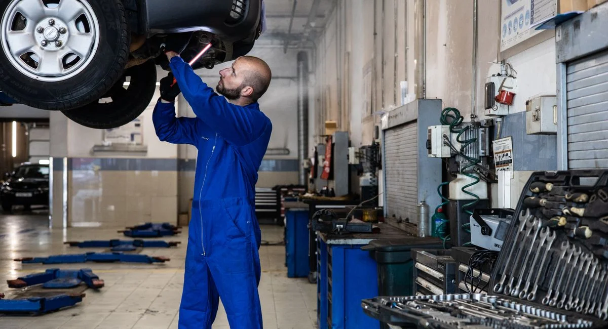 Mechanic inspecting a raised car in an auto workshop for maintenance and repair services.