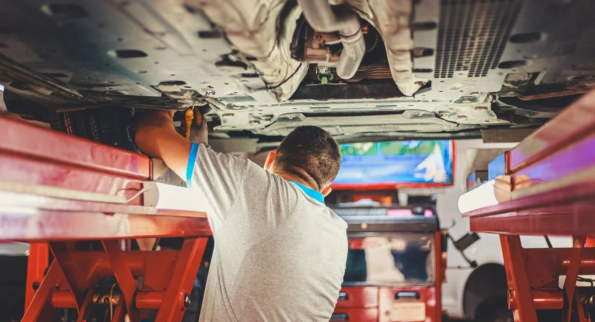 A mechanic works under a lifted car in an auto repair shop, adjusting parts.