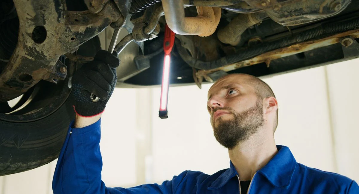 Mechanic focusing on vehicle maintenance under a car lift in a garage.