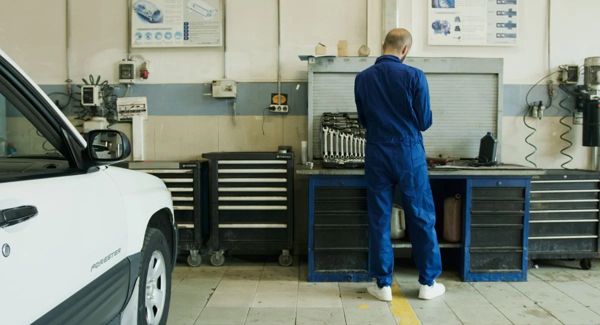Mechanic in blue overalls inspecting a white car in a well-equipped garage.