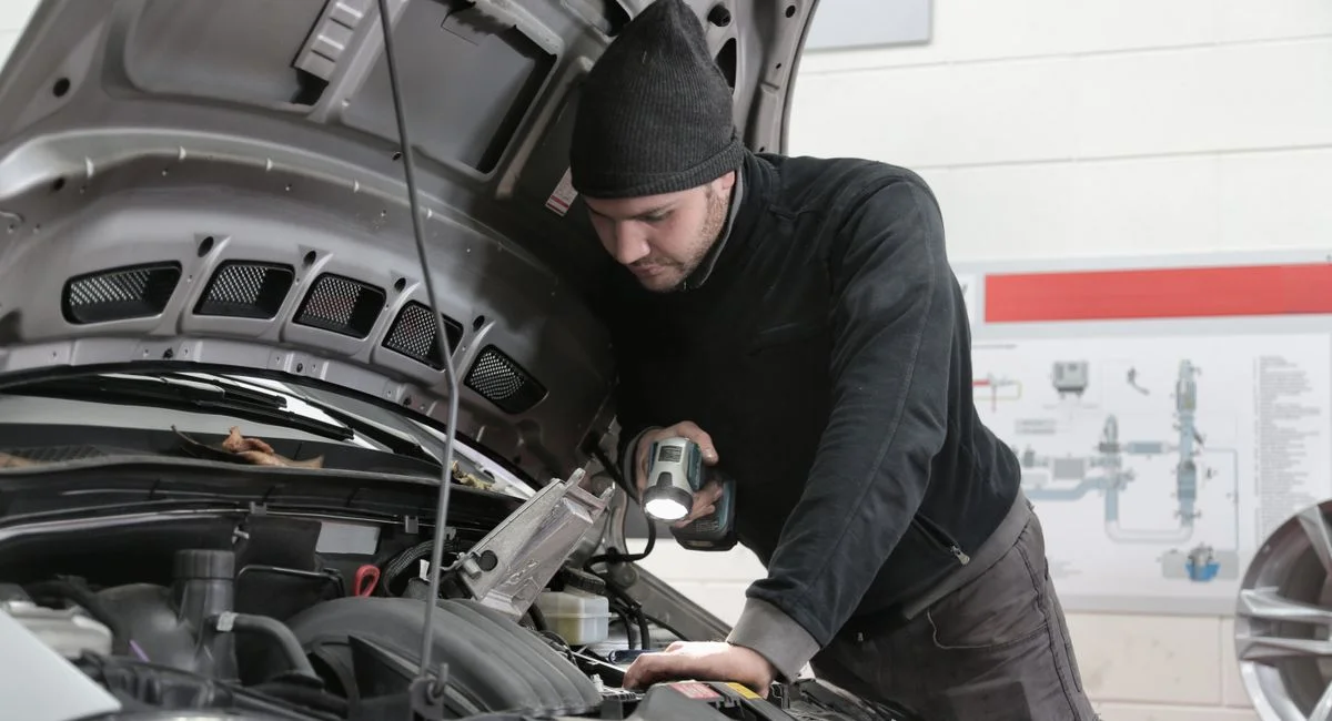A mechanic closely inspects a car engine in a garage using a flashlight, ensuring proper maintenance.