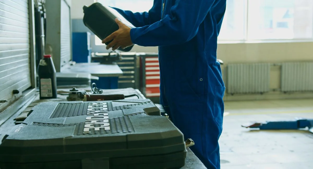 Mechanic in blue overalls holding engine oil container in a workshop environment, enhancing maintenance efficiency.