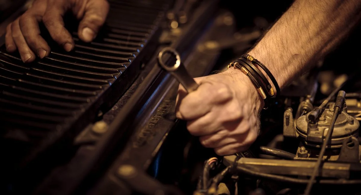 Close-up view of a mechanic's hands working on a car engine with a wrench in an industrial setting.