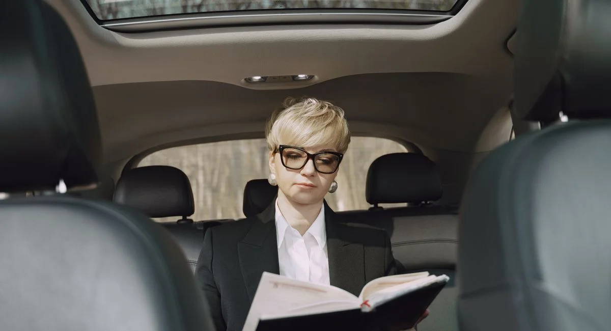 From below of concentrated female entrepreneur in elegant formal clothes sitting on backseat while reading memos in notebook 