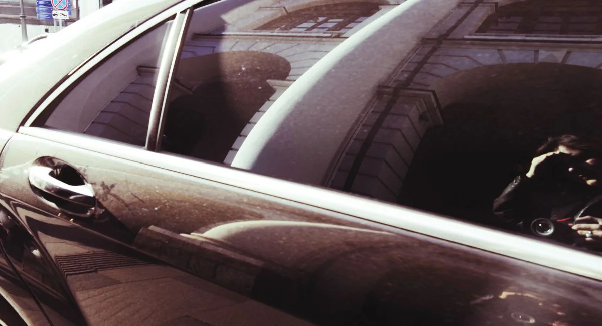 Urban scene with a building reflected on a car window and a photographer's reflection.