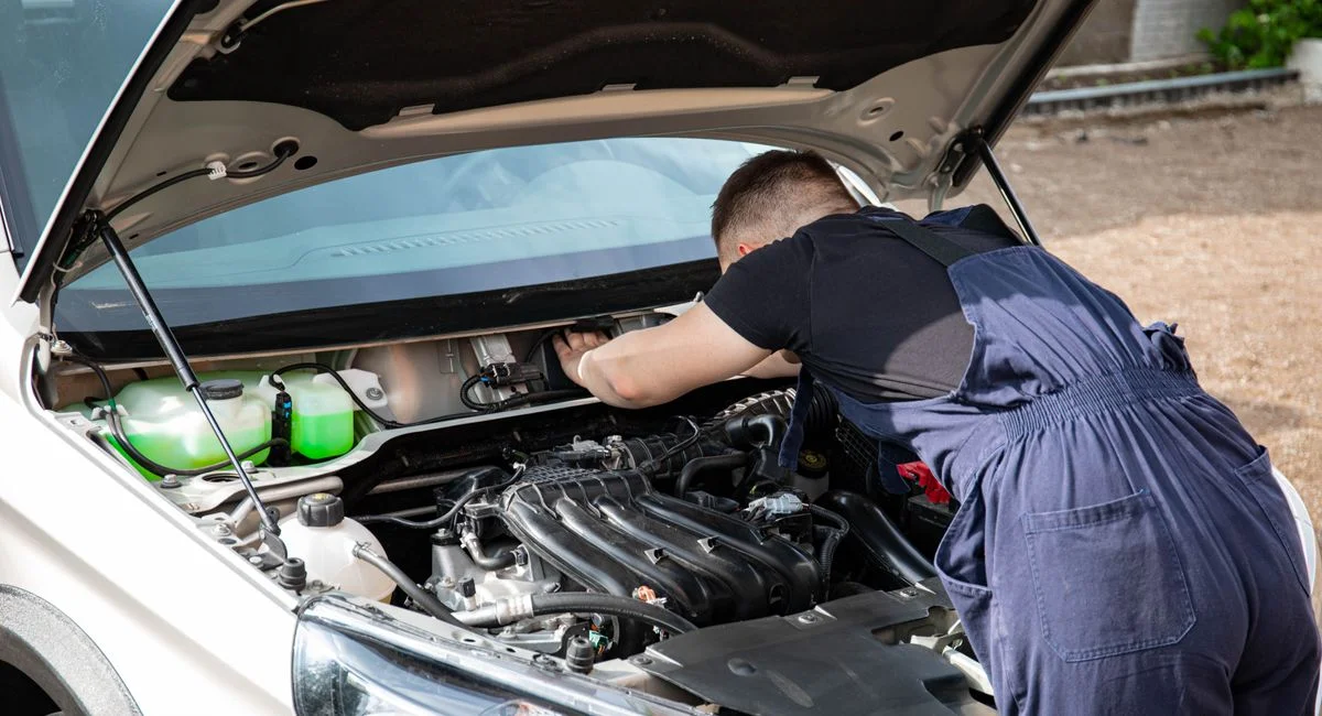 A skilled mechanic works on a car engine in an outdoor setting, showcasing automotive maintenance.