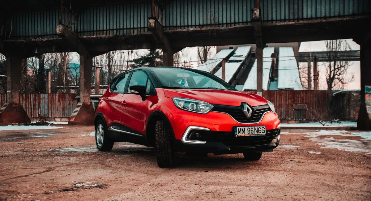 Striking red Renault Captur parked in a rugged industrial setting under a bridge.