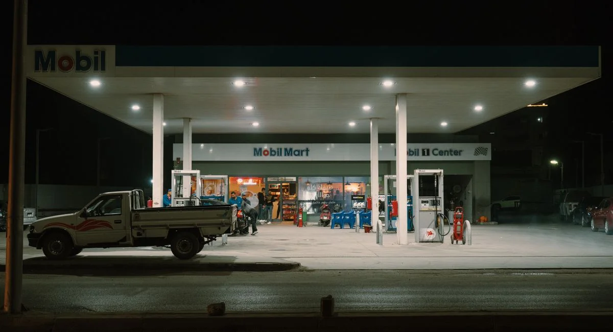 A Mobil gas station with vehicles and people under bright lights at night.