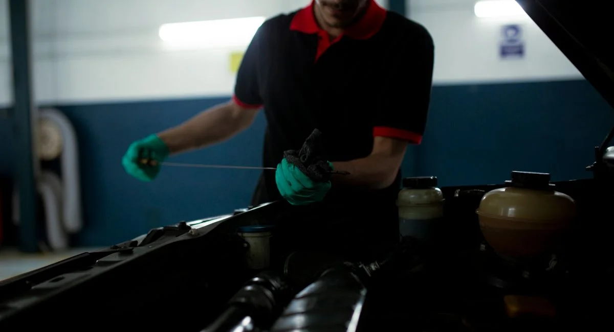 Mechanic examining a car engine's oil level using a dipstick in a garage setting.