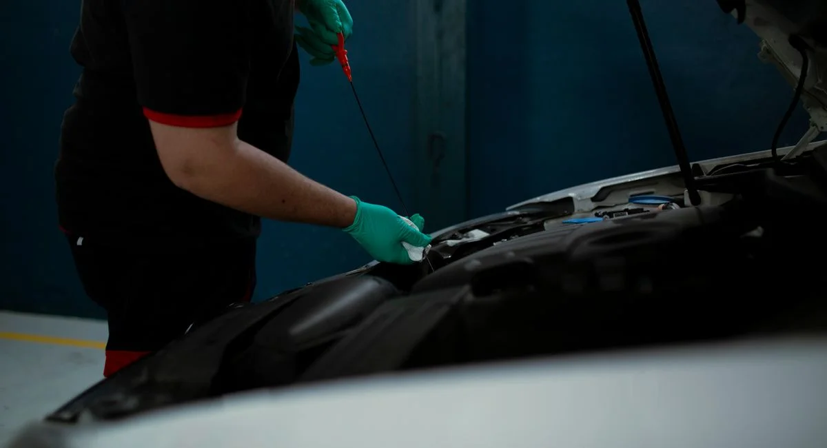 Mechanic in gloves checking engine oil level in a vehicle at an indoor workshop.