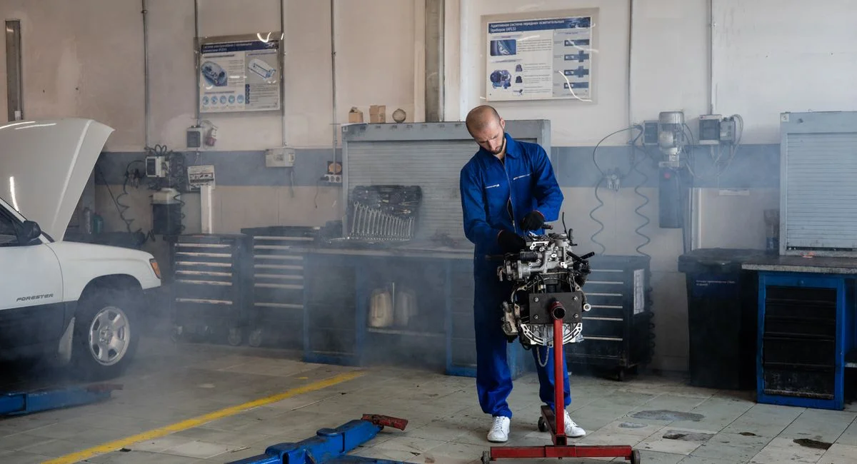 A mechanic repairing a car engine in a busy auto repair shop with tools around.