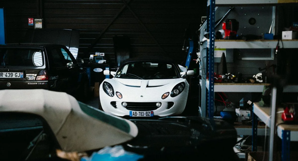 A classic white sports car is parked inside a dimly lit garage in Montigny-le-Bretonneux.