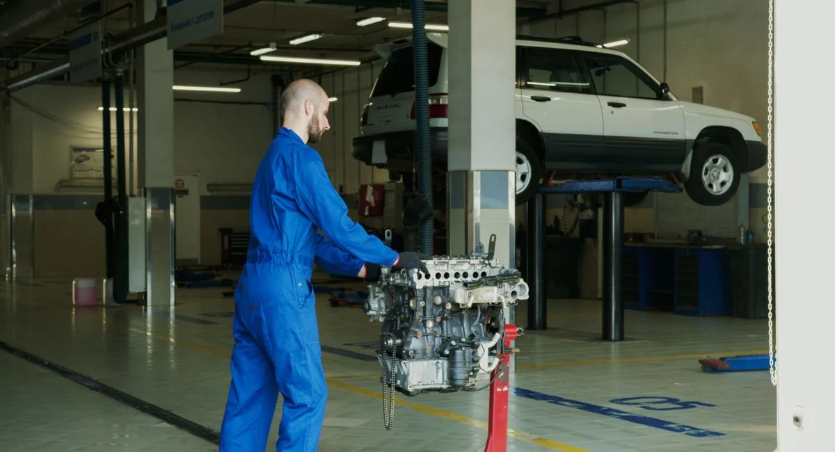 Mechanic in blue overalls working on an engine in an indoor automotive garage.