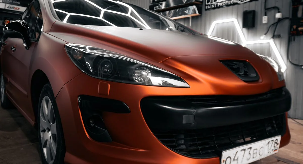 Stylish matte orange car displayed in a contemporary auto workshop setting with neon lighting.