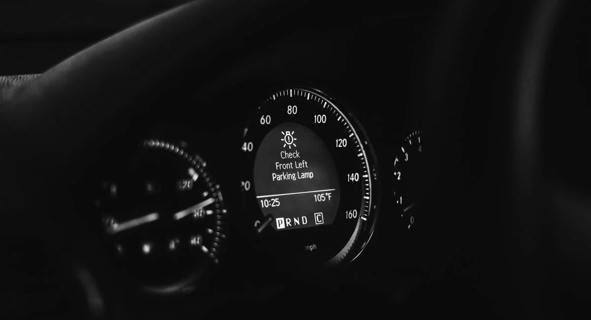 Close-up of a car dashboard in black and white, highlighting speedometer and warning lights.